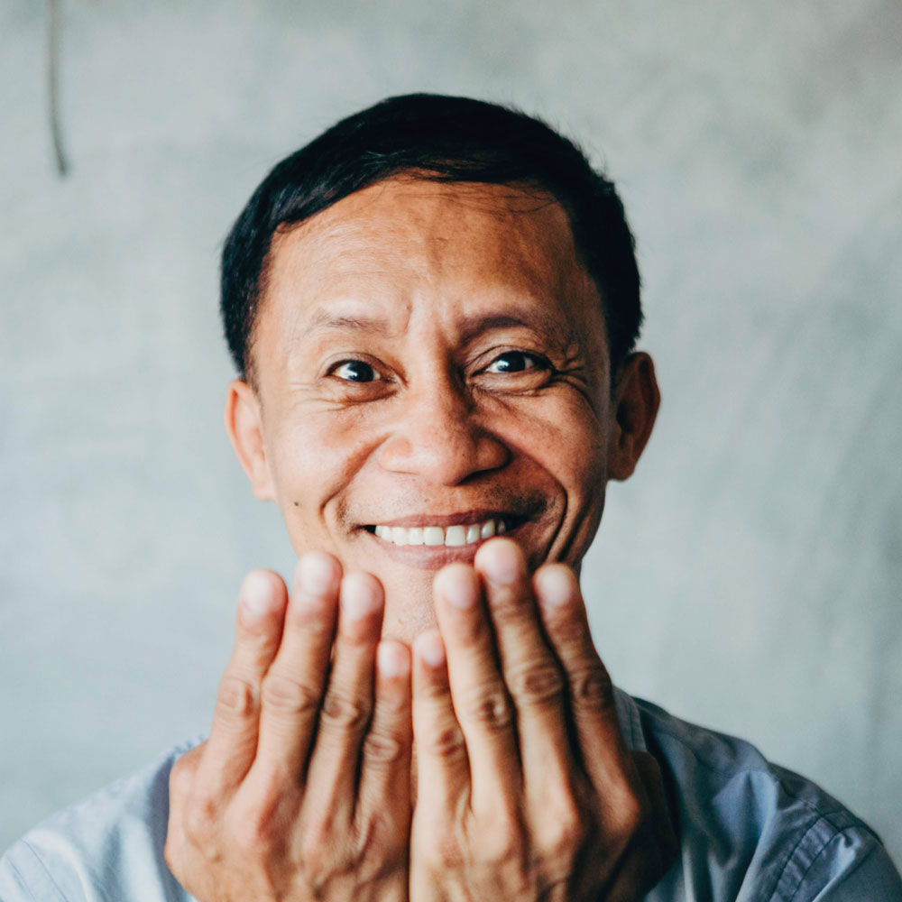 A man is smiling and holding two hands up in front of his face